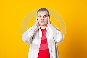 Portrait handsome, peaceful, tranquil, looking relaxed, young man covering his ears, observing. Hear no evil concept.