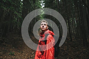 Portrait of a handsome pensive caucasian young man looking up, feeling curious and adventurous, wearing a red waterproof coat and
