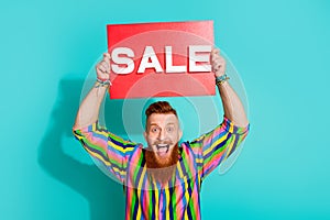 Portrait of handsome red hair bearded man in striped shirt hold red poster sale offer message isolated on aquamarine