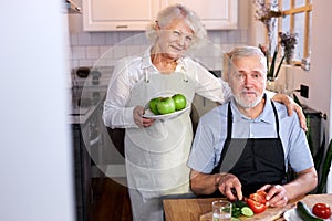 portrait of handsome senior man carving vegetables and wife holding plate with apples