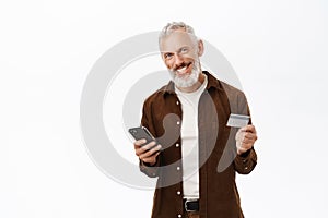 Portrait of handsome senior man, caucasian old guy using smartphone and holding credit card, shopping online, paying