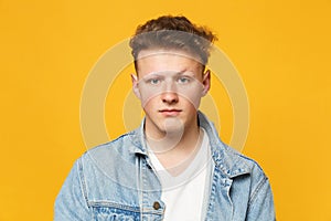 Portrait of handsome serious young man wearing denim casual clothes looking camera isolated on yellow orange wall