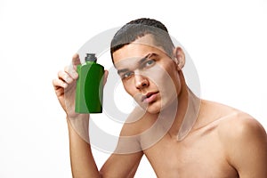 Portrait of handsome shirtless young man holding bottle with shampoo, showers gel against white studio background