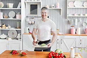 Portrait of handsome smiling man chopping vegetables in the kitchen. The concept of eco-friendly products for cooking.