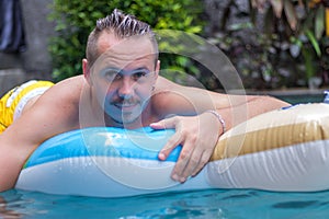 Portrait of handsome smiling man on the inflatable mattress in swimming pool at sunny day. Bali.