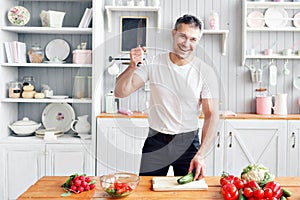 Portrait of handsome smiling man at kitchen. cooking and home concept - close up of male hand chopping cucumber on