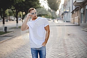 Portrait of handsome smiling stylish model. Man dressed in white T-shirt. Fashion male posing on the street background