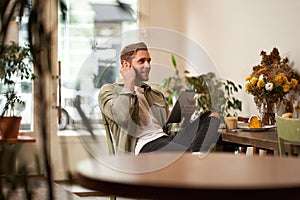 Portrait of handsome smiling young man, sitting in coffee shop, using digital tablet, video chats with someone from a