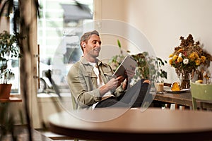 Portrait of handsome smiling young man, sitting in coffee shop, using digital tablet, video chats with someone from a