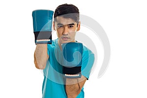 Portrait of handsome sportsman in blue gloves and uniform practicing boxing on camera isolated on white background