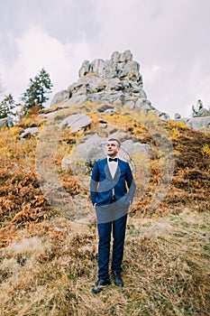 Portrait of handsome stylish groom in blue suit with a rocky natural landscape as background