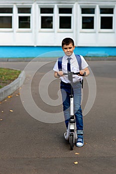 Portrait of a handsome stylish and young schoolboy in a white shirt, blue tie and a backpack with a scooter
