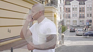 Portrait of handsome successful confident bald middle eastern man speaking by the cell phone standing on the street in