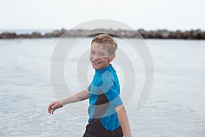 Portrait of handsome teen boy running in neoprene swimsuit in sea