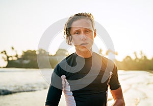 Portrait of a handsome teen boy surfing rashguard on the sand Indian ocean beach with sunset on background. Happy teen time and