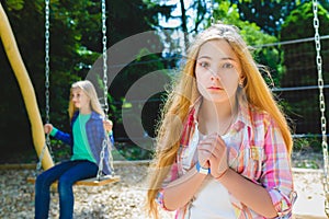 Portrait handsome teen pleading or beging at park. On the background other girl riding a swing photo