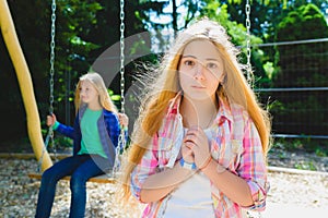 Portrait handsome teen pleading or beging at park. On the background other girl riding a swing photo