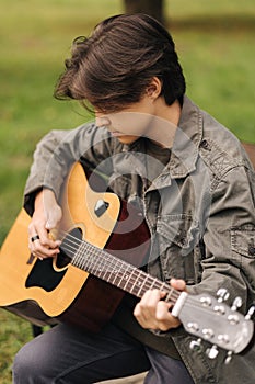 Portrait of handsome teenage boy playing guitar outdoor. Boy using classic guitar. Male alone making music