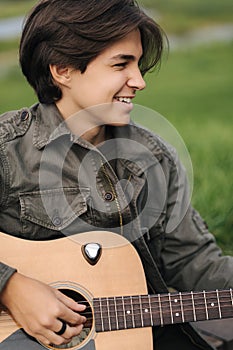 Portrait of handsome teenage boy playing guitar outdoor. Boy using classic guitar. Male alone making music