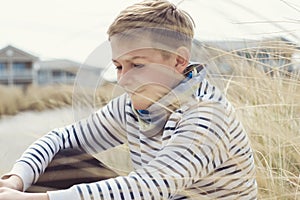 Portrait of handsome teenage boy sitting and smiling on white sand on Baltic sea beach