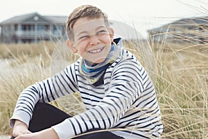 Portrait of handsome teenage boy sitting and smiling on white sand on Baltic sea beach