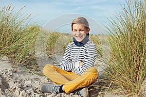 Portrait of handsome teenager boy sitting on white sand on beach of Baltic sea