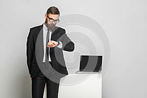 Portrait of handsome thoughful bearded young businessman in corporated format wear in black suit are standing and checking time on