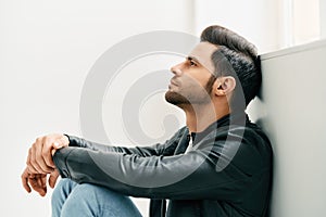 Portrait of handsome thoughtful man sitting on floor leaning to the wall