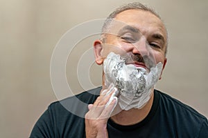 Portrait of handsome white-haired beared middle-aged man applying shaving foam to trim his beard