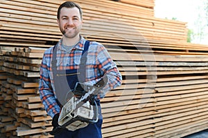 Portrait of a handsome worker choosing the best wooden boards. Carpenter standing next to a big stack of wood bars in a