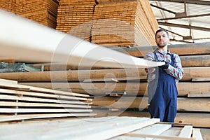 Portrait of a handsome worker choosing the best wooden boards. Carpenter standing next to a big stack of wood bars in a