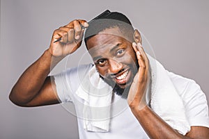 Portrait of handsome young african american black man combing his hair in bathroom. Isolated over grey background