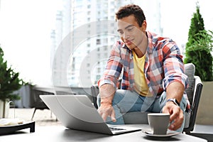 Portrait of handsome young -American man with laptop and cup of drink in outdoor cafe