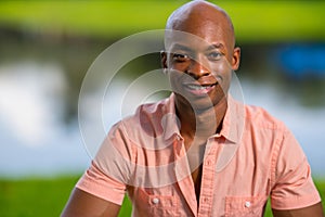 Portrait handsome young African American man smiling at camera. Man wearing a pink button shirt unbuttoned half way