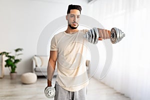 Portrait of handsome young Arab guy exercising with dumbbells at home during covid-19 lockdown, selective focus