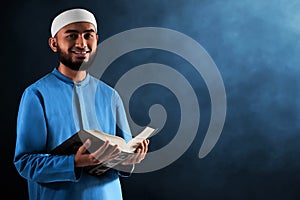 Portrait of handsome young asian muslim man with beard holding holy book quran and smile