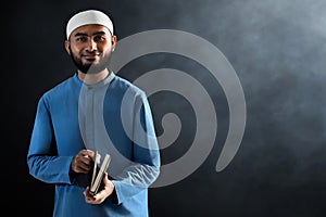 Portrait of handsome young asian muslim man with beard posing, hold holy book quran