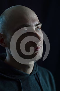 Portrait of a handsome young bald man with blue eyes who in the dim light looks thoughtfully away