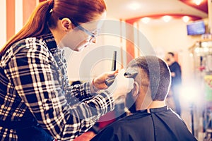 Portrait of handsome young bearded caucasian man getting trendy haircut in modern barber shop.