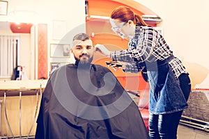 Portrait of handsome young bearded caucasian man getting trendy haircut in modern barber shop.