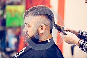 Portrait of handsome young bearded caucasian man getting trendy haircut in modern barber shop.