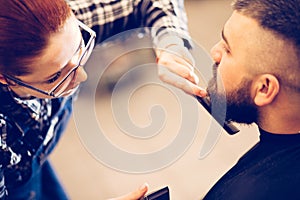 Portrait of handsome young bearded caucasian man getting trendy haircut in modern barber shop.