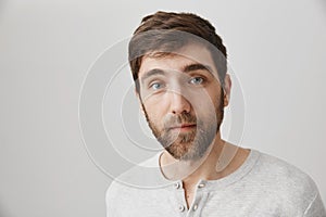 Portrait of handsome young bearded male model with calm and relaxed expression, glancing at camera while standing