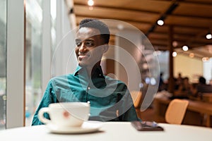 Portrait of handsome young black man in coffee shop looking through window