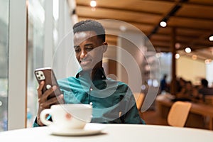 Portrait of handsome young black man in coffee shop using phone