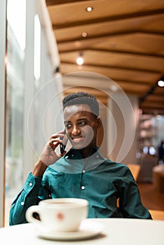 Portrait of handsome young black man in coffee shop using phone