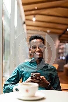 Portrait of handsome young black man in coffee shop using phone