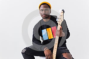 Portrait handsome young black man dressed in jeans and sweatshirt with guitar on white background. Street fashion and