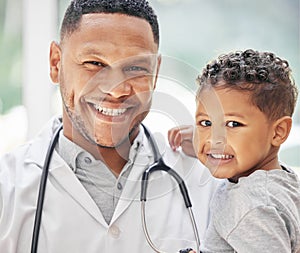 Portrait of handsome young black paediatrician holding adorable little boy in hands, cute child and doctor smiling