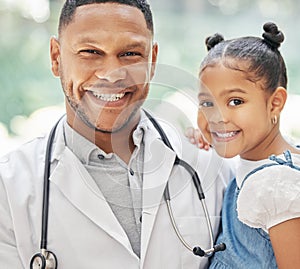 Portrait of handsome young black paediatrician holding adorable little girl in hands, cute child and doctor smiling
